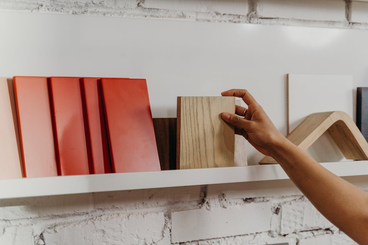 A hand selecting a wooden sample from a display shelf featuring various construction materials.