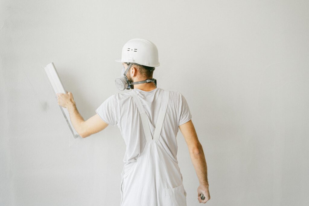 pexels photo 5493658 5493658 Back view of a construction worker in safety gear plastering a white wall.